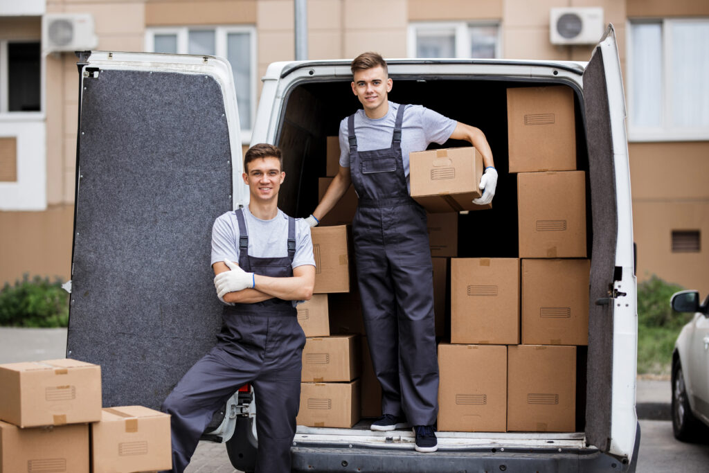 Two young movers wearing uniforms are unloading the van full of boxes. House move, mover service.